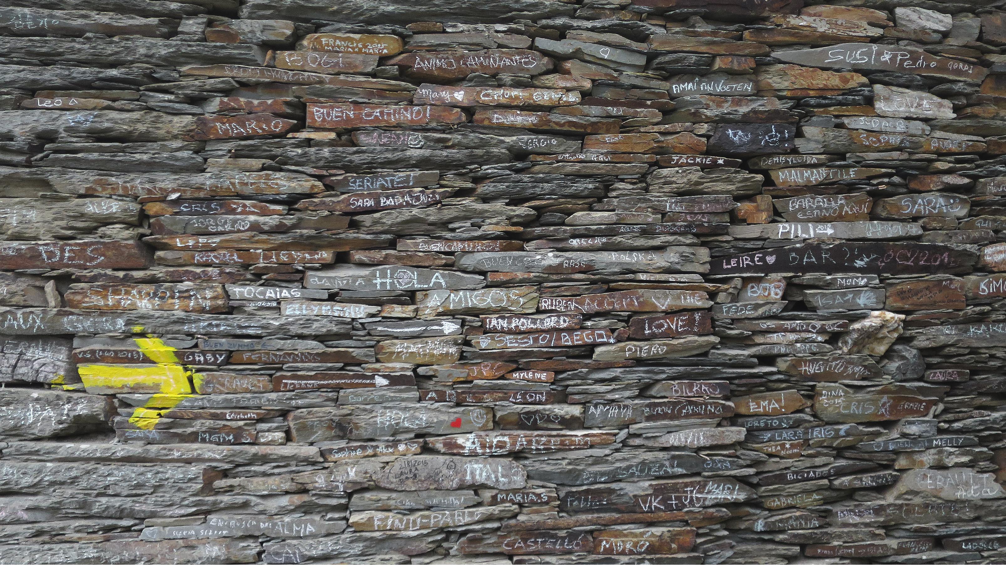 Pared de piedras en el Camino de Santiago con flecha amarilla